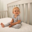 Sealy Cozy Dreams Waterproof Fitted Crib Mattress Pad infant sitting in crib plush knit surface hypoallergenic comfortable waterproof flat secure fit Thumbnail