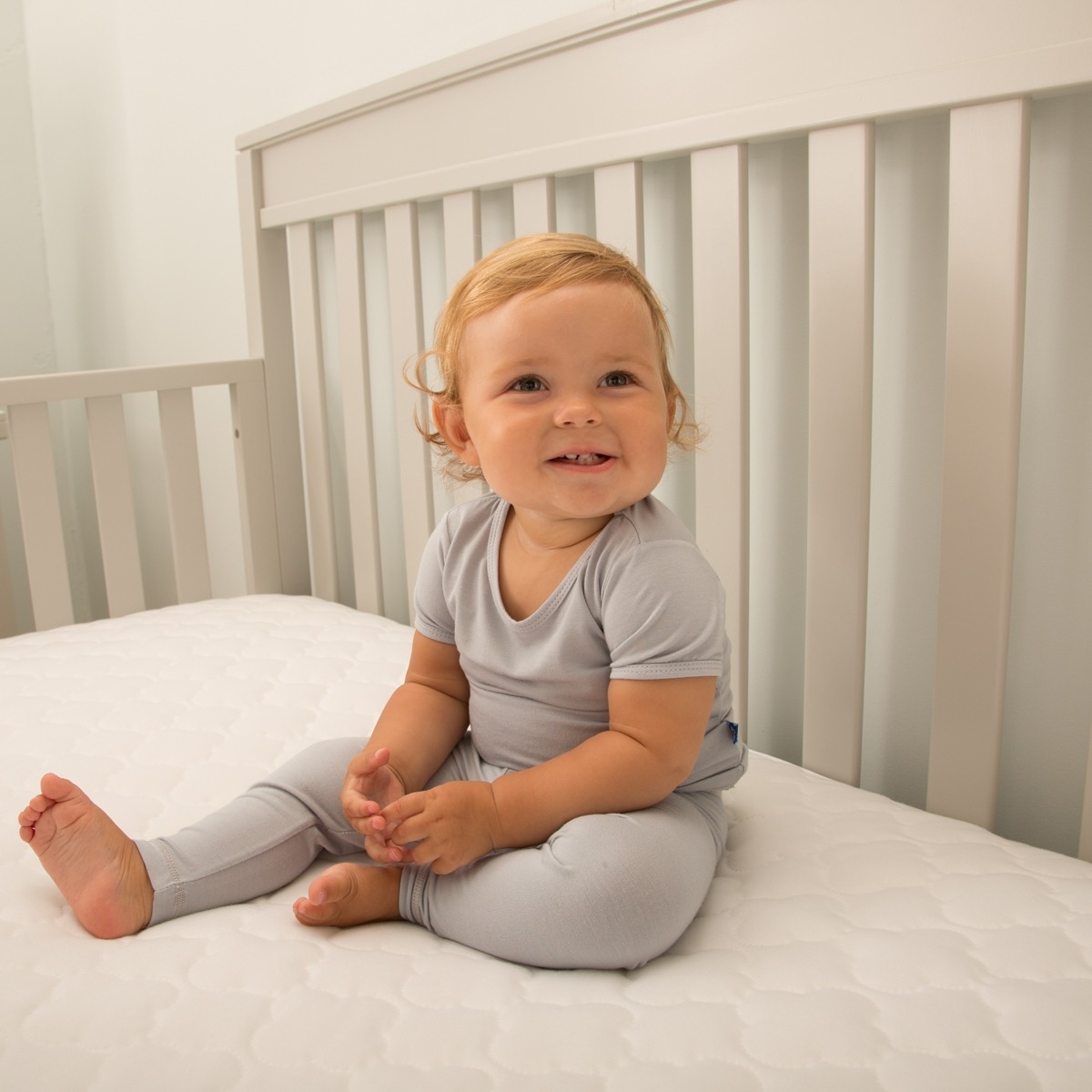 Sealy Cozy Dreams Waterproof Fitted Crib Mattress Pad infant sitting in crib plush knit surface hypoallergenic comfortable waterproof flat secure fit